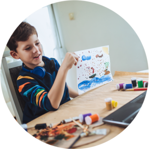 young boy holding up artwork to show teacher in online learning